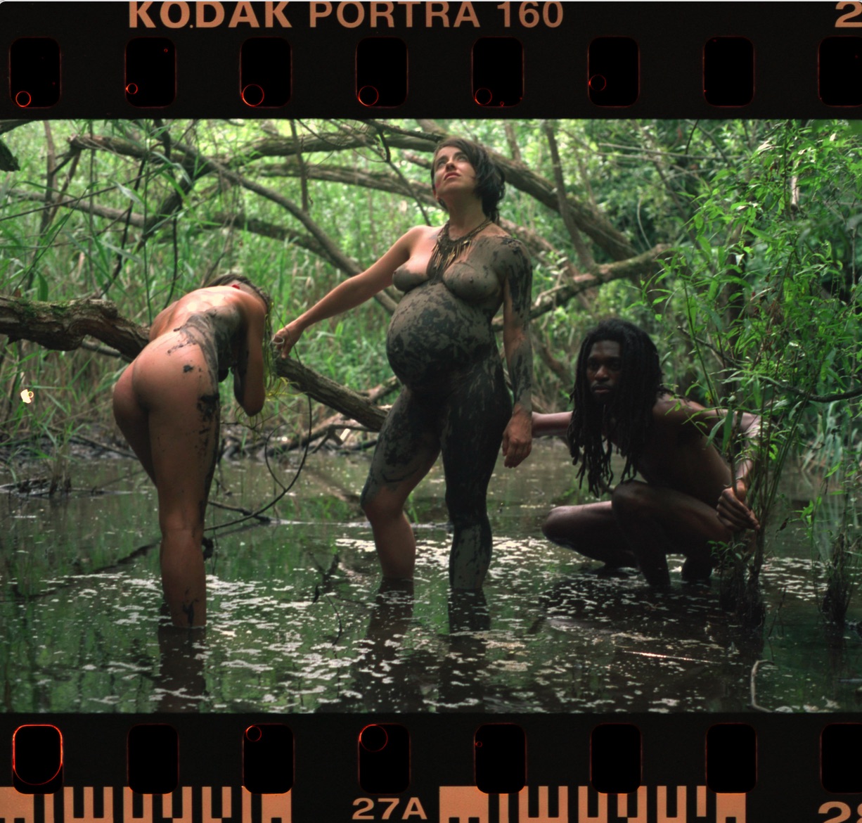Three performers in a wetland during Mud Joy